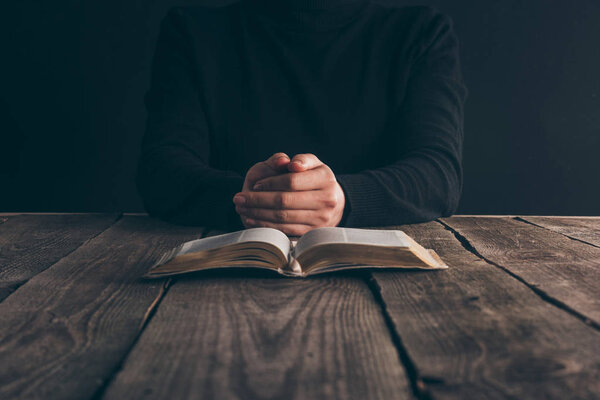 обрезанный образ монахини, сидящей за столом с библией и молящейся
 
