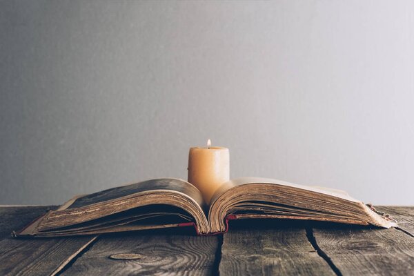 open holy bible with candle on wooden table