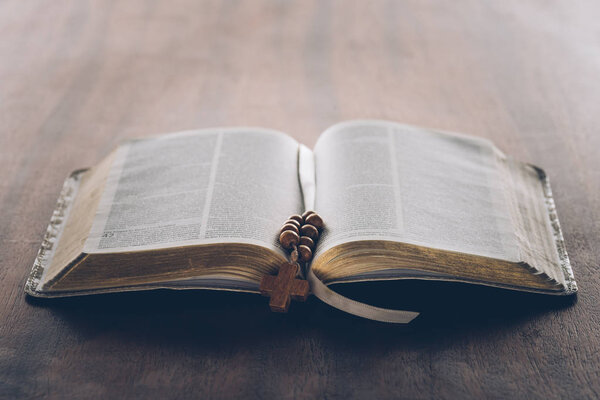 open holy bible and rosary with cross on wooden table  