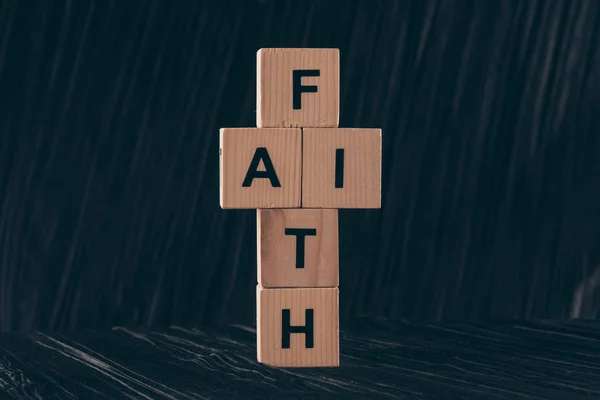 黒いテーブルの上の単語の信仰と十字架の形の木製キューブ — ストック写真