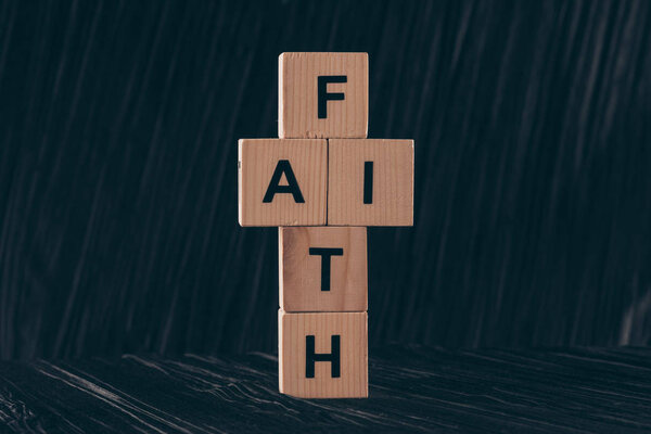 деревянные кубики в форме креста со словом "Вера" на черном столе
