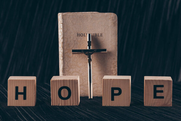 wooden cubes with word Hope and bible with cross on black table