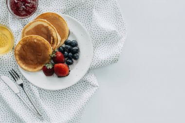 top view of plate of delicious pancakes with berries on white table