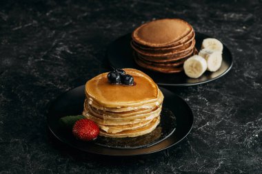 plates with stacks of tasty pancakes with fruits on black table clipart