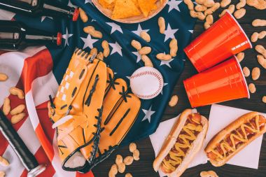 Amerikan bayrağı sosisli sandviç, plastik bardak, fıstık, bira şişeleri, beyzbol topu ve eldiven sopayla Üstten Görünüm