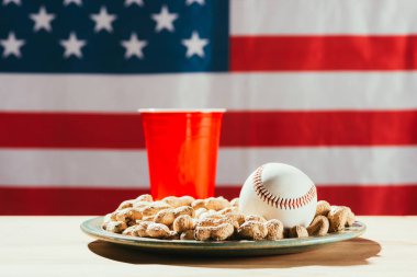 close-up view of baseball ball on plate with peanuts, red plastic bottle and american flag behind clipart