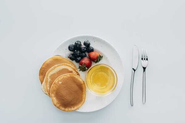 top view of pancakes with berries and maple syrup on white table