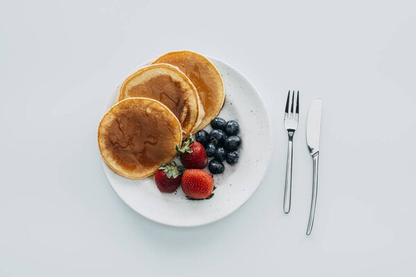 top view of plate of pancakes with berries and cutlery on white table