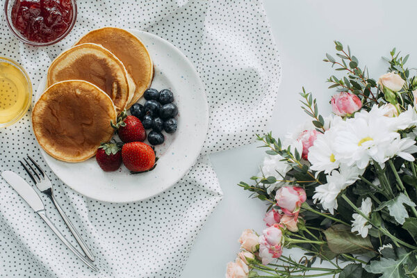top view of tasty breakfast with pancakes and flowers bouquet on white