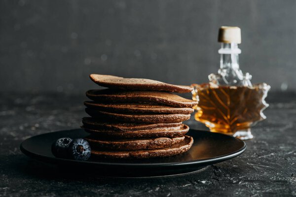 stacked chocolate pancakes with bottle of maple syrup