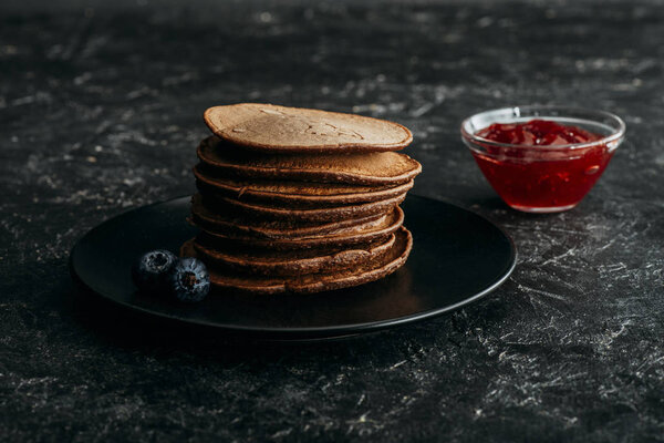 stacked chocolate pancakes with blueberries and bowl of jam