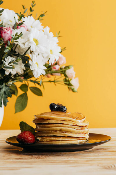 stacked pancakes with berries and syrup on table with flowers in vase