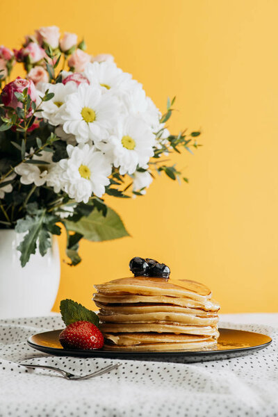 delicious stacked pancakes with berries and syrup on table with flowers in vase