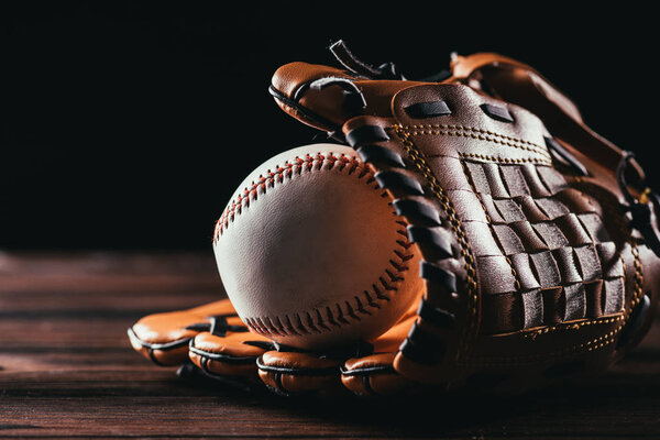 close-up view of white leather baseball ball and glove on wooden table