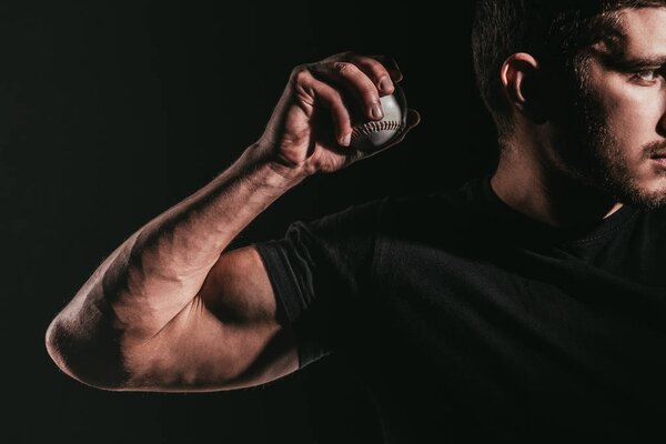 обрезанный снимок молодого мускулистого спортсмена, держащего бейсбольный мяч изолированный на черном
