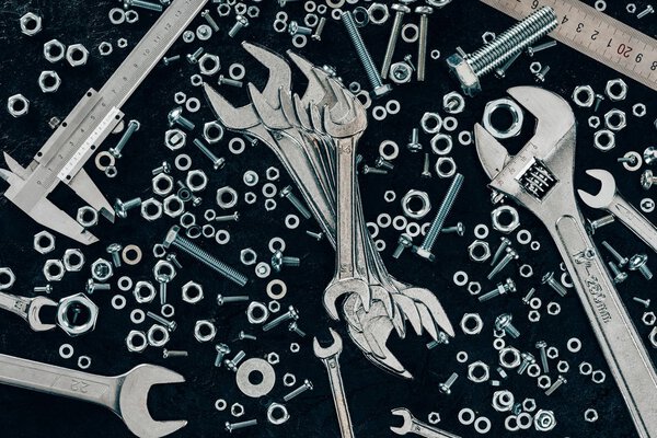 top view of arranged metal ruler, clinchers, screws and vernier caliper on dark tabletop