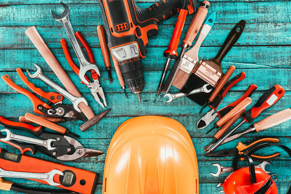 flat lay with various carpentry equipment with helmet in middle on blue wooden surface