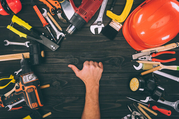 partial view of male hand showing thumb up with carpentry equipment around on wooden surface