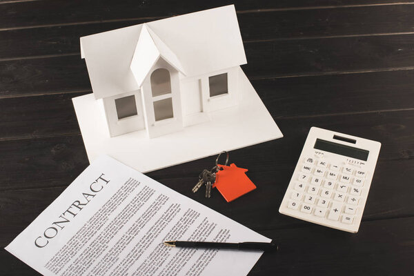 Концепция покупки дома с контрактом, ключами, калькулятором и макетом над деревянным столом
