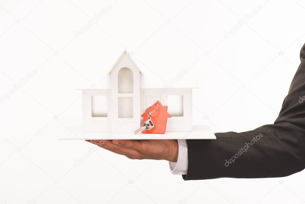 cropped image of hand holding maquette of house with key isolated on white
