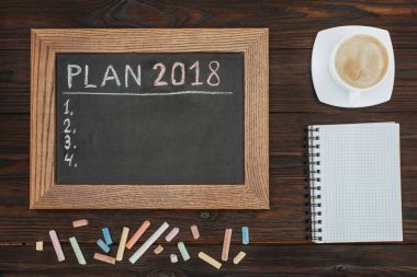 flat lay with empty chalkboard, cup of coffee, blank notebook and chalks on dark wooden tabletop clipart