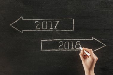 cropped shot of female hand with chalk and 2017, 2018 signs on dark wooden surface  clipart