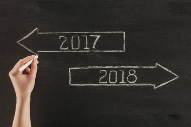 cropped shot of female hand with chalk and 2017, 2018 signs on dark wooden surface  clipart