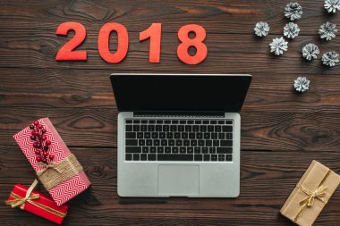 dizüstü bilgisayar, sarılmış hediyeler ve 2018 numaraları ahşap yüzey üzerinde düz lay