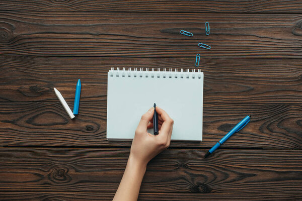 partial view of woman with pencil in hand writing in notebook on wooden tabletop