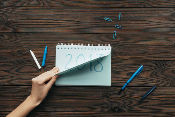cropped shot of woman tearing notebook paper with 2018 year sign on wooden tabletop