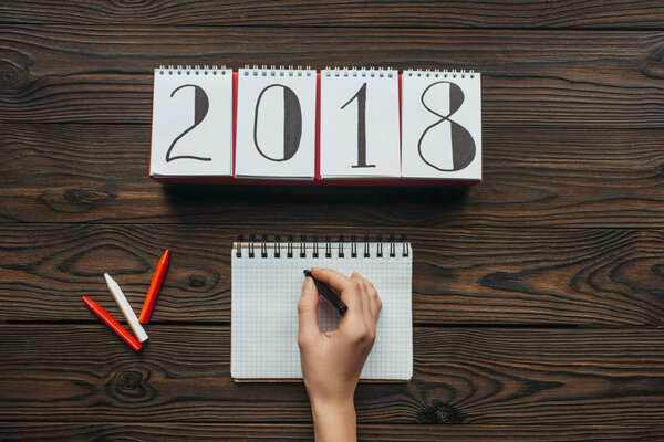 частичный вид женщины с карандашом в руке, записной книжкой на деревянном столе
