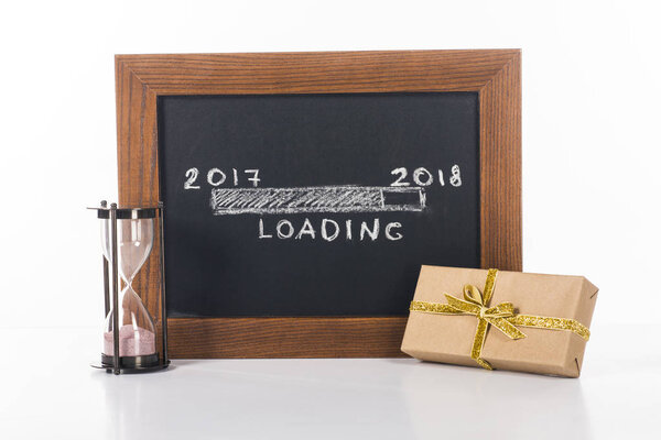 close up view of chalkboard with 2017 to 2018 loading lettering with hourglass and gift near by isolated on white