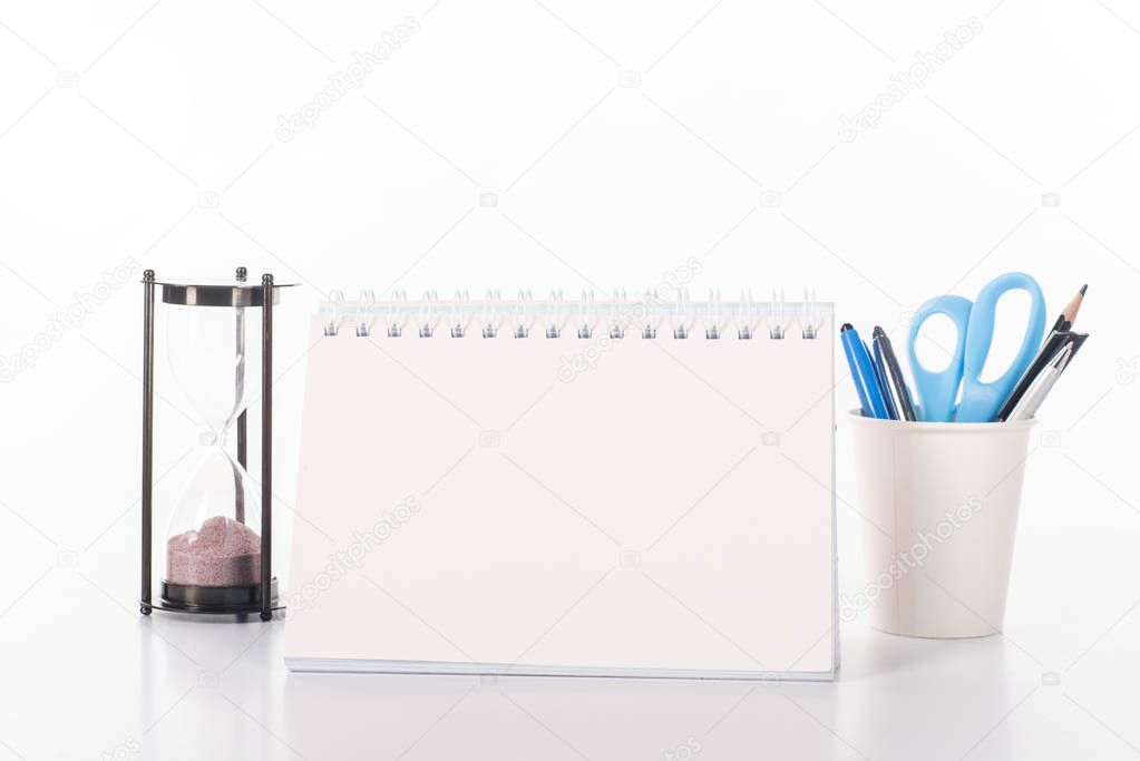 close up view of blank calendar, sand clock and office supplies isolated on white