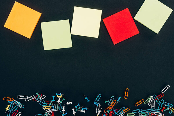 top view of various colorful blank notes and paper clips on black 