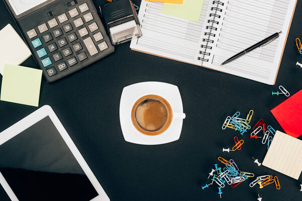 top view of digital tablet with blank screen, cup of coffee, calculator and office supplies on black