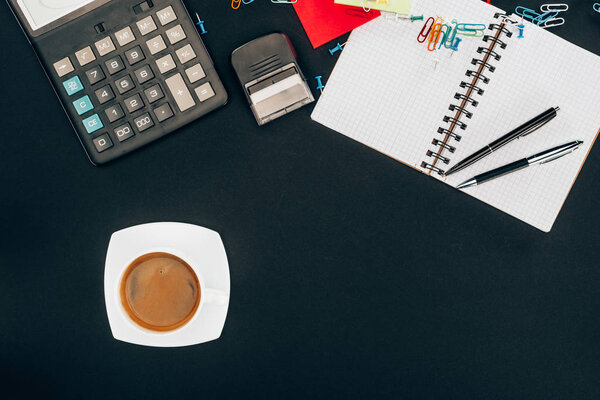 top view of cup of coffee, calculator and office supplies on black