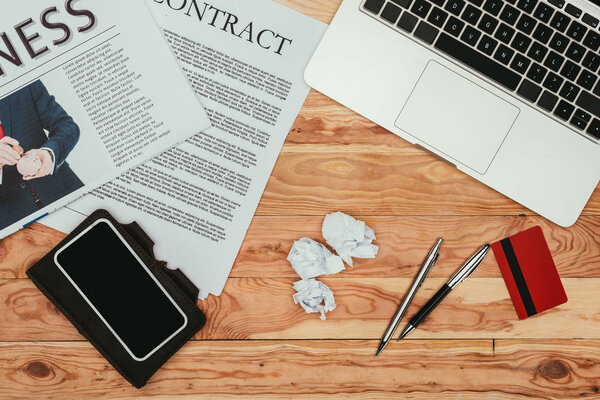 top view of smartphone with blank screen, contract newspaper, laptop and credit card on wooden table