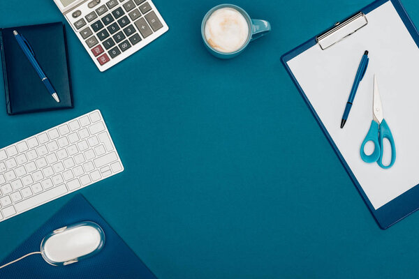 top view of blank clipboard with pen and scissors, computer mouse and keyboard and calculator on blue