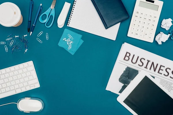 top view of business newspaper, digital tablet, calculator and office supplies on blue