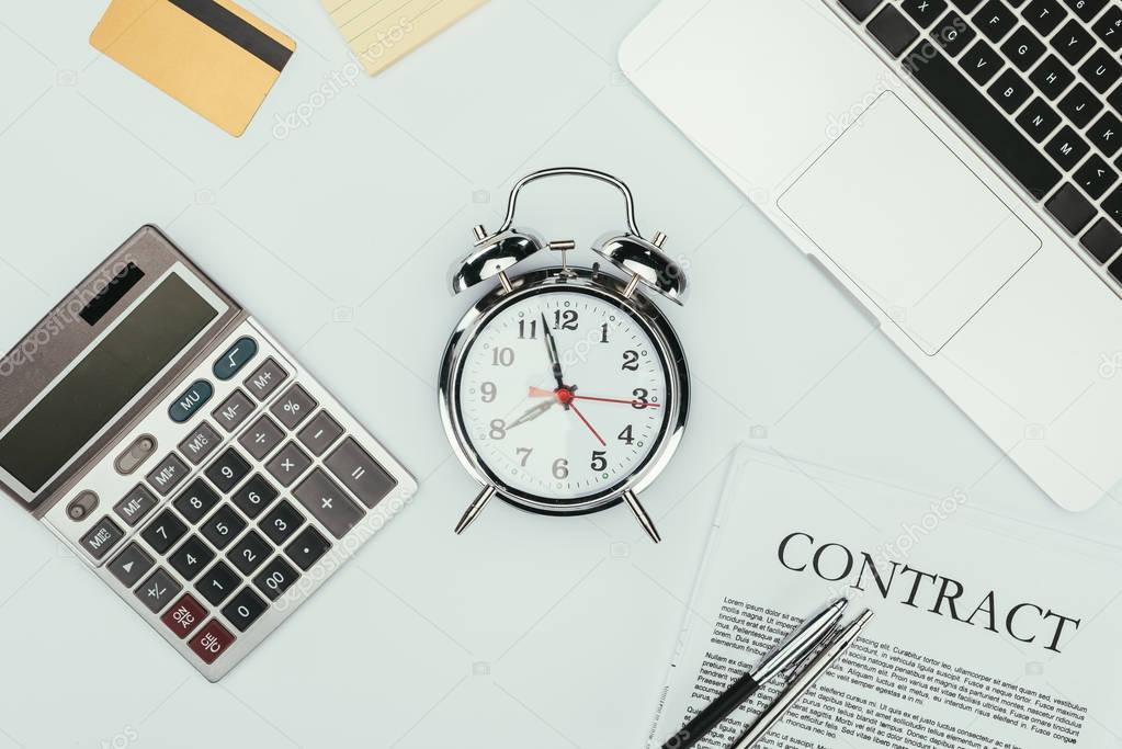 top view of alarm clock, calculator, contract with pens, credit card and laptop on white