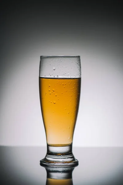 single glass with light fresh beer on gray reflecting table