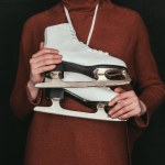 Cropped image of woman in brown sweater holding skates isolated on black