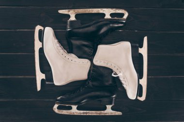 top view of pairs of white and black skates on wooden surface clipart