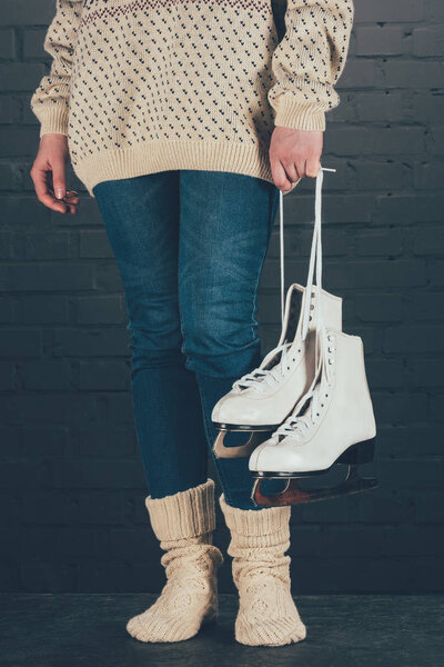обрезанный образ женщины, стоящей и держащей коньки в шнурках
