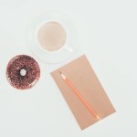 Draufsicht auf Donut mit Tasse Kaffee und leerem Kraftpapier auf weißer Tischplatte