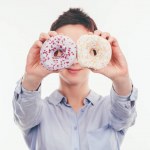 Smiling woman covering eyes with tasty doughnuts isolated on white