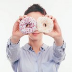 Mujer sonriente cubriendo los ojos con sabrosas rosquillas aisladas en blanco