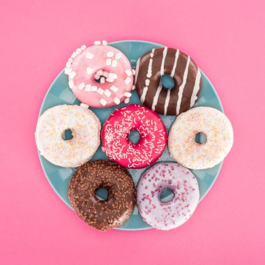 top view of various glazed doughnuts on plate isolated on pink clipart