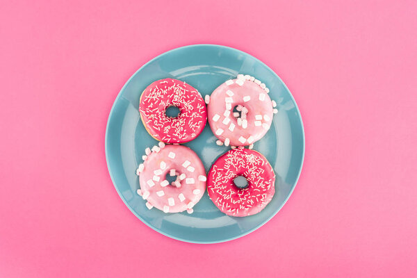 вид сверху на глазированные пончики на тарелке изолированы на розовый
