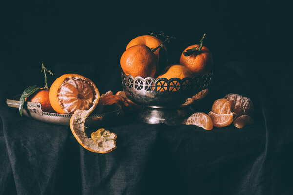 close up view of fresh mandarins in metal bowl on table with dark tablecloth